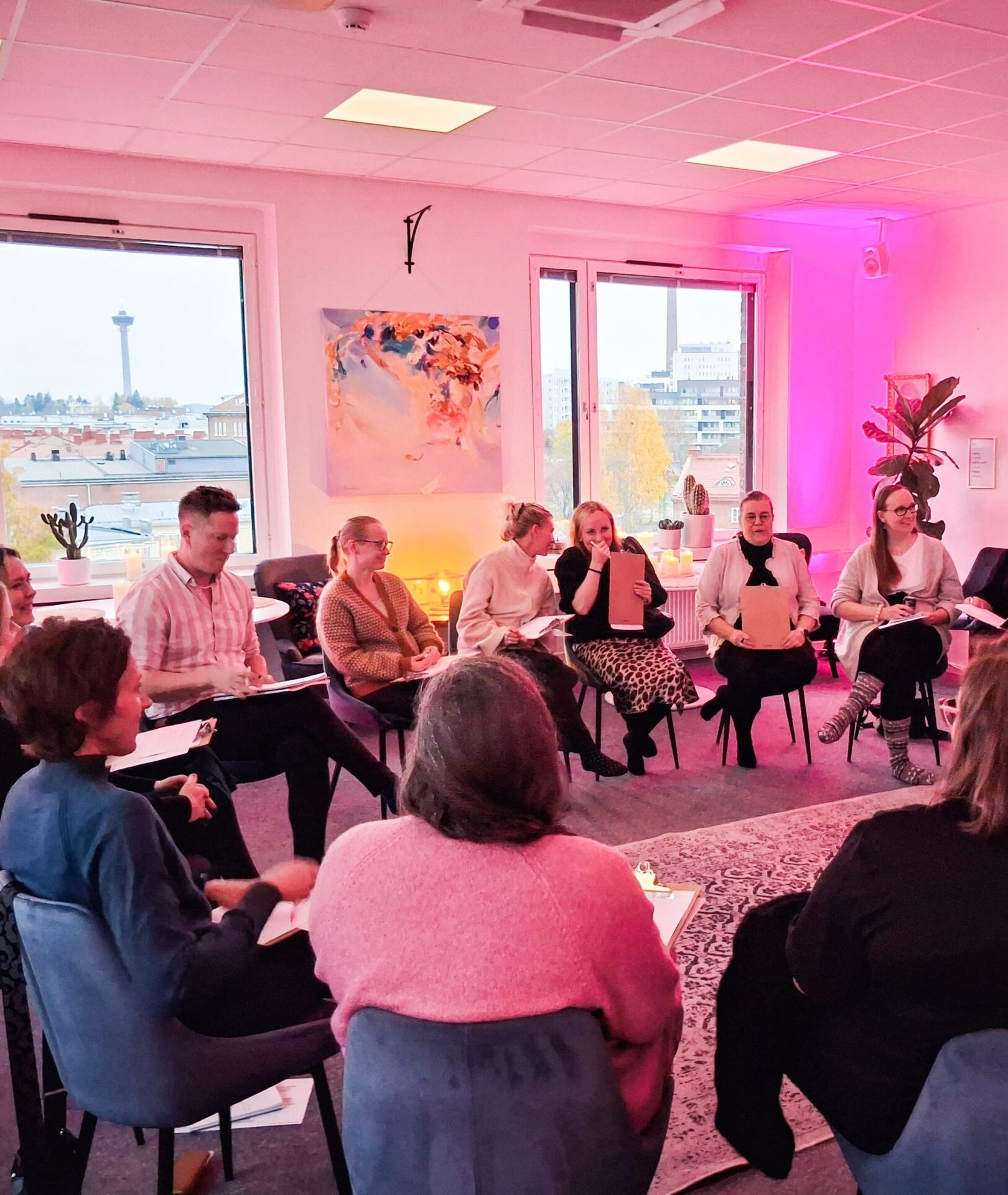 HR-asiantuntijoita ja esihenkilöitä osallistumassa Kasvussa Oy:n HR-Dialogiin Tampereella. Ryhmä istuu keskusteluringissä inspiroivassa tilassa, jossa käydään avointa dialogia työelämän kehittämisestä ja vuorovaikutuksesta. Taustalla näkyy Tampereen kaupunkimaisema ja Näsinneula.